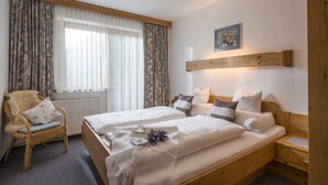 A room with two beds, a wicker chair, a wooden headboard, and a radiator.