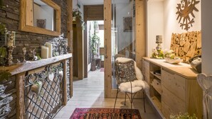 A narrow hallway with a wooden door leading to a room. A chair with a white cushion is placed against the wall.