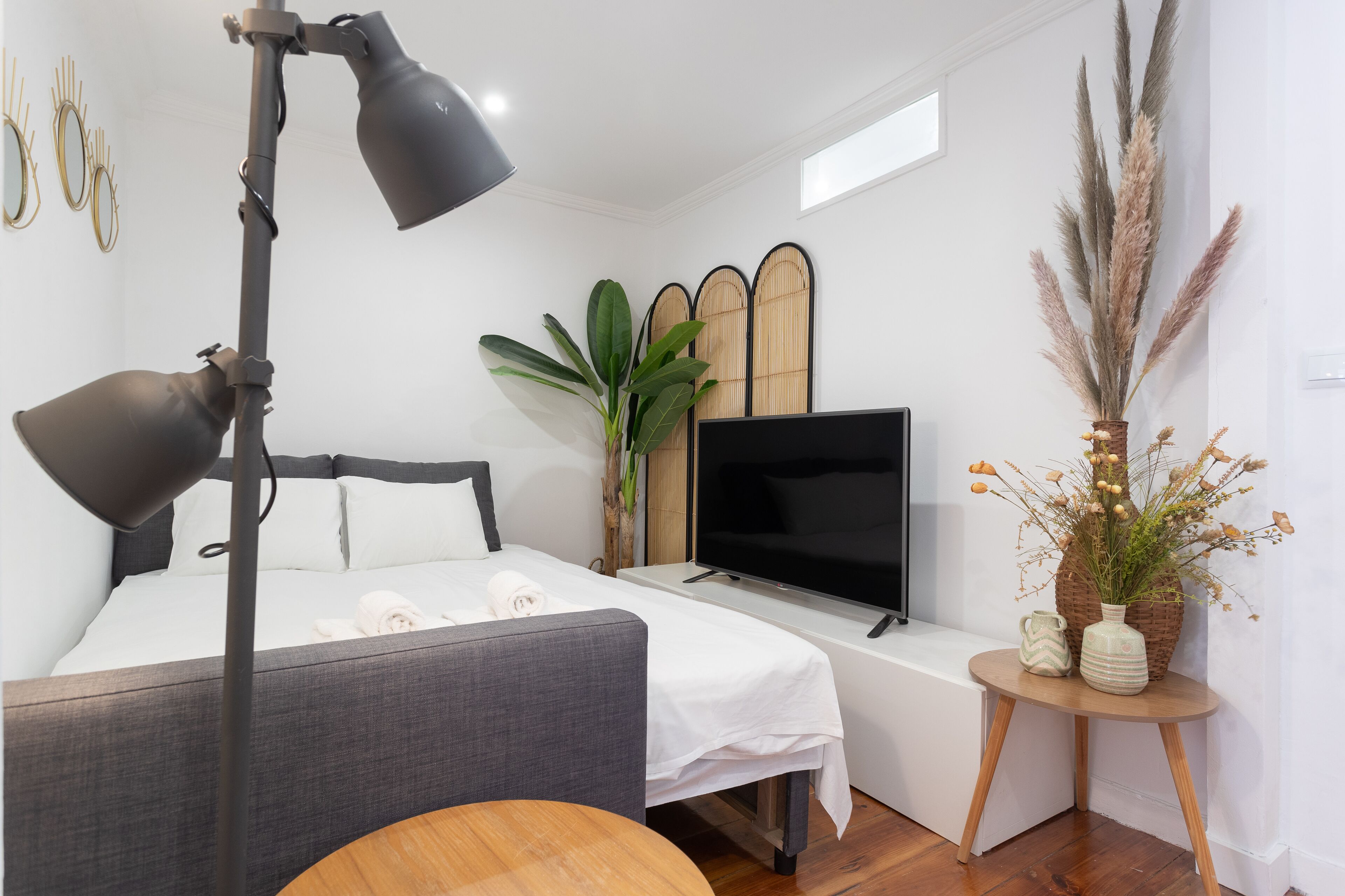 A modern hotel room with a bed, a TV, a desk, and a lamp.