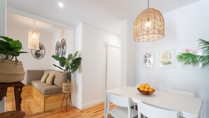 Un salon moderne avec un canapé blanc, une table à manger avec des chaises et un luminaire suspendu.