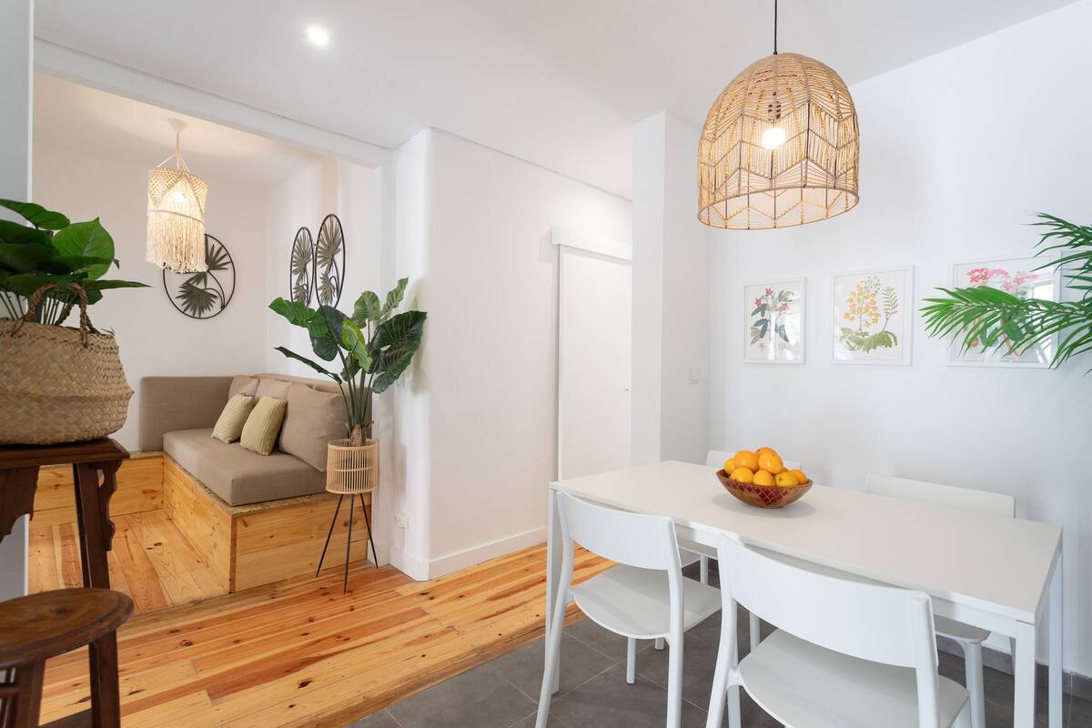 Una sala de estar moderna con un sofá blanco, una mesa de comedor con sillas y una lámpara colgante.