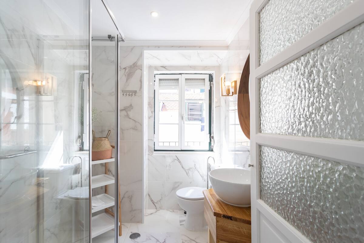 Un baño con cabina de ducha de vidrio, un lavabo blanco y suelo de baldosas de mármol.