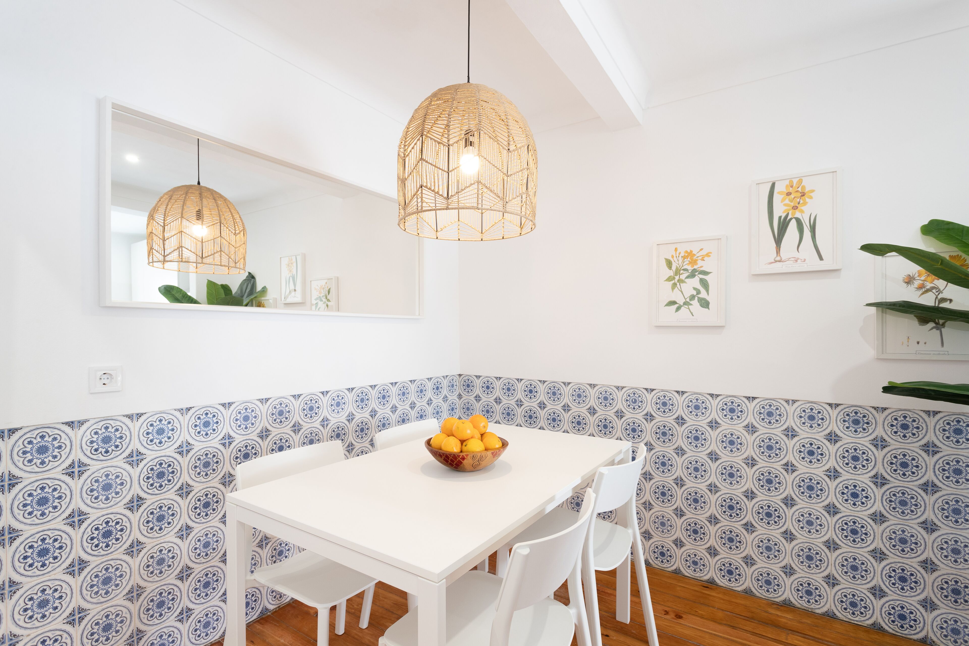 Un comedor con una mesa blanca, sillas blancas, un bol de fruta y una lámpara colgante.