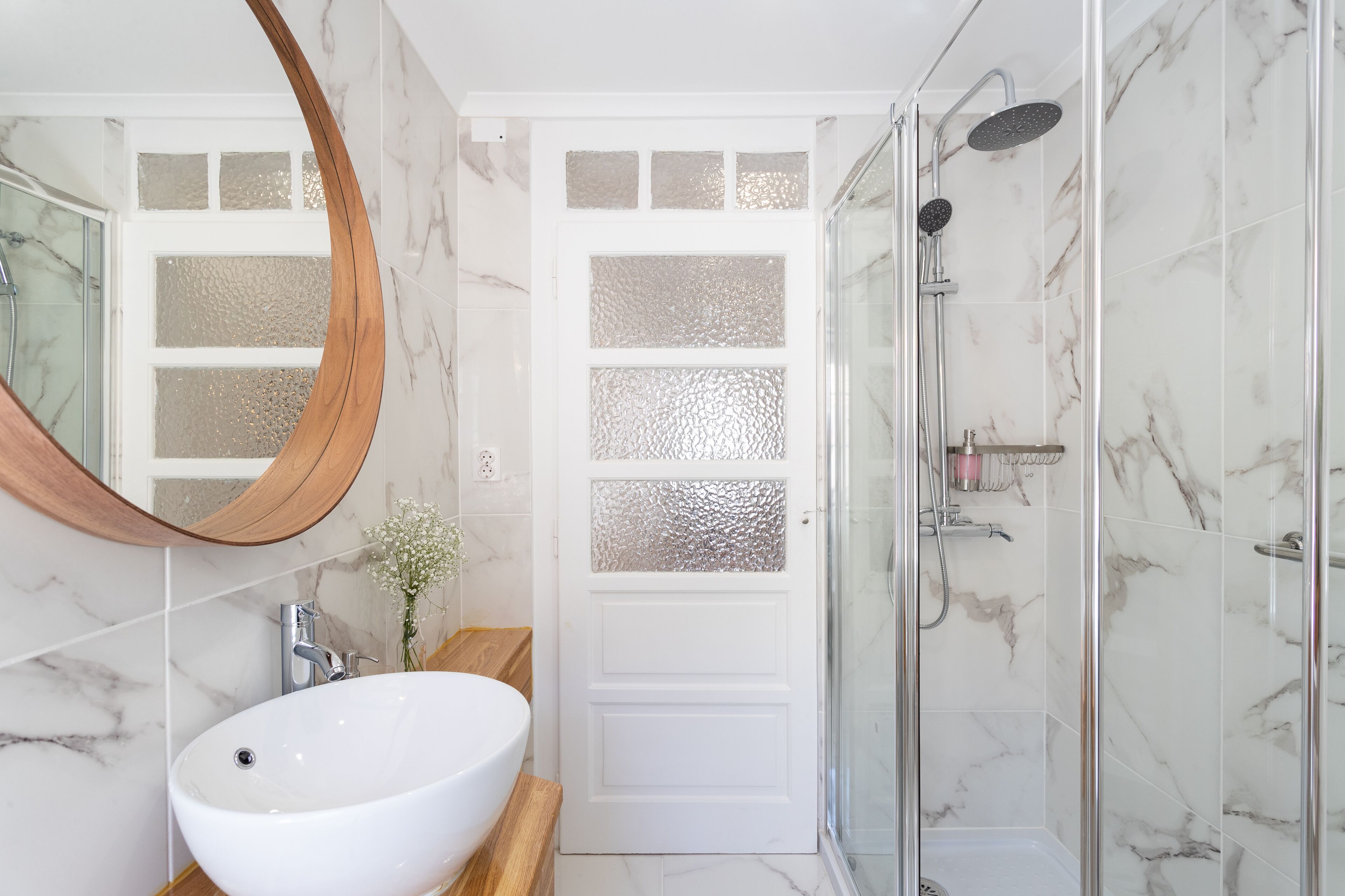 A bathroom with a white sink, a wooden vanity, a glass shower enclosure, and a frosted glass door.
