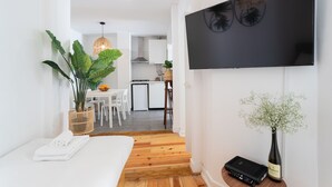 Un salon moderne avec un téléviseur à écran plat, une grande plante, une petite table avec des chaises et un plancher en bois.