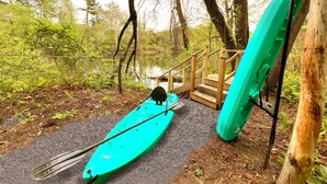A kayak and paddle leaning against a wooden structure in a forested area with a wooden staircase leading to a dock.