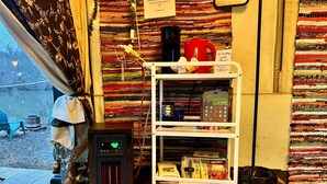 A cozy room with a heater, a shelf with various items, and a view of the outside.