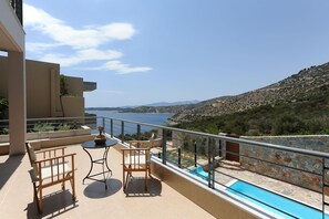 Un balcon avec une piscine, du mobilier d’extérieur et une vue sur la mer et les collines.