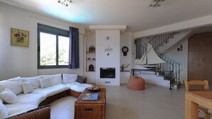 Ein modernes Wohnzimmer mit einem weißen Ecksofa, einem Korbtisch, einem Kamin, einer Treppe und einem Essbereich.