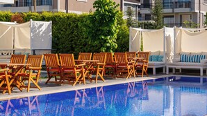 A poolside area with wooden chairs and a sofa, surrounded by white canopies.