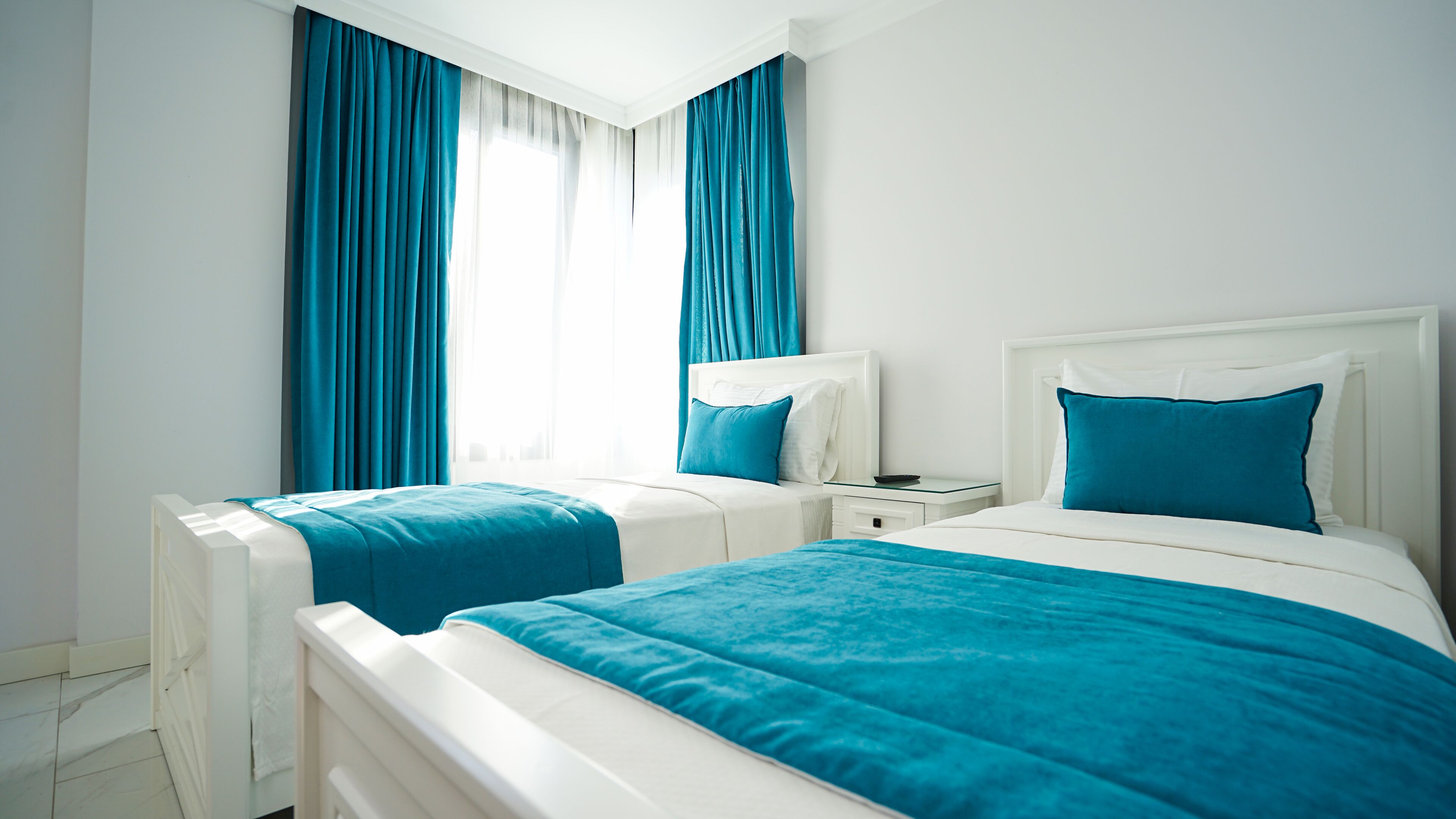 Habitación de hotel con dos camas, cabeceros blancos y ropa de cama azul.