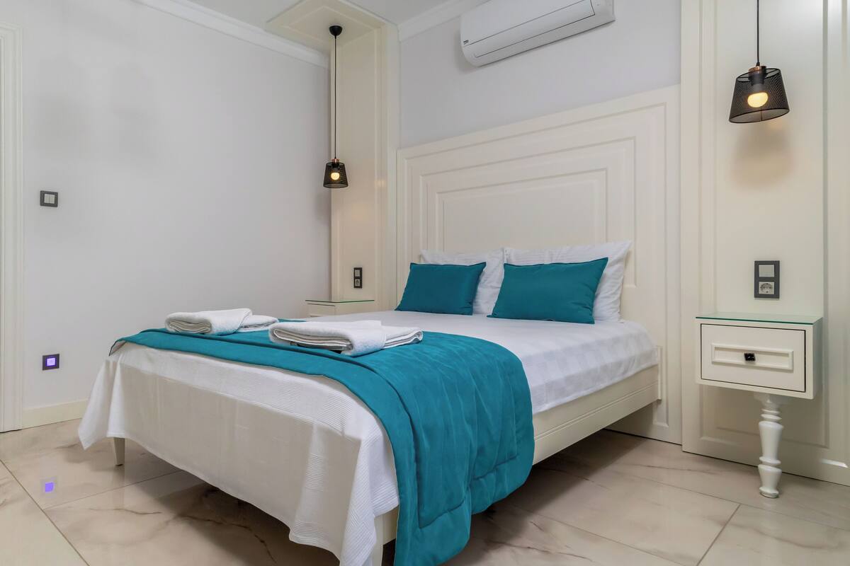 Ein modernes Hotelzimmer mit einem ordentlich bezogenen Bett, einem Glastisch, einem Nachttisch und einer Hängelampe.