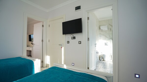 A hotel room with two beds, a television mounted on the wall, and a bathroom visible through an open door. - Cunda Garden (Ayvalik)