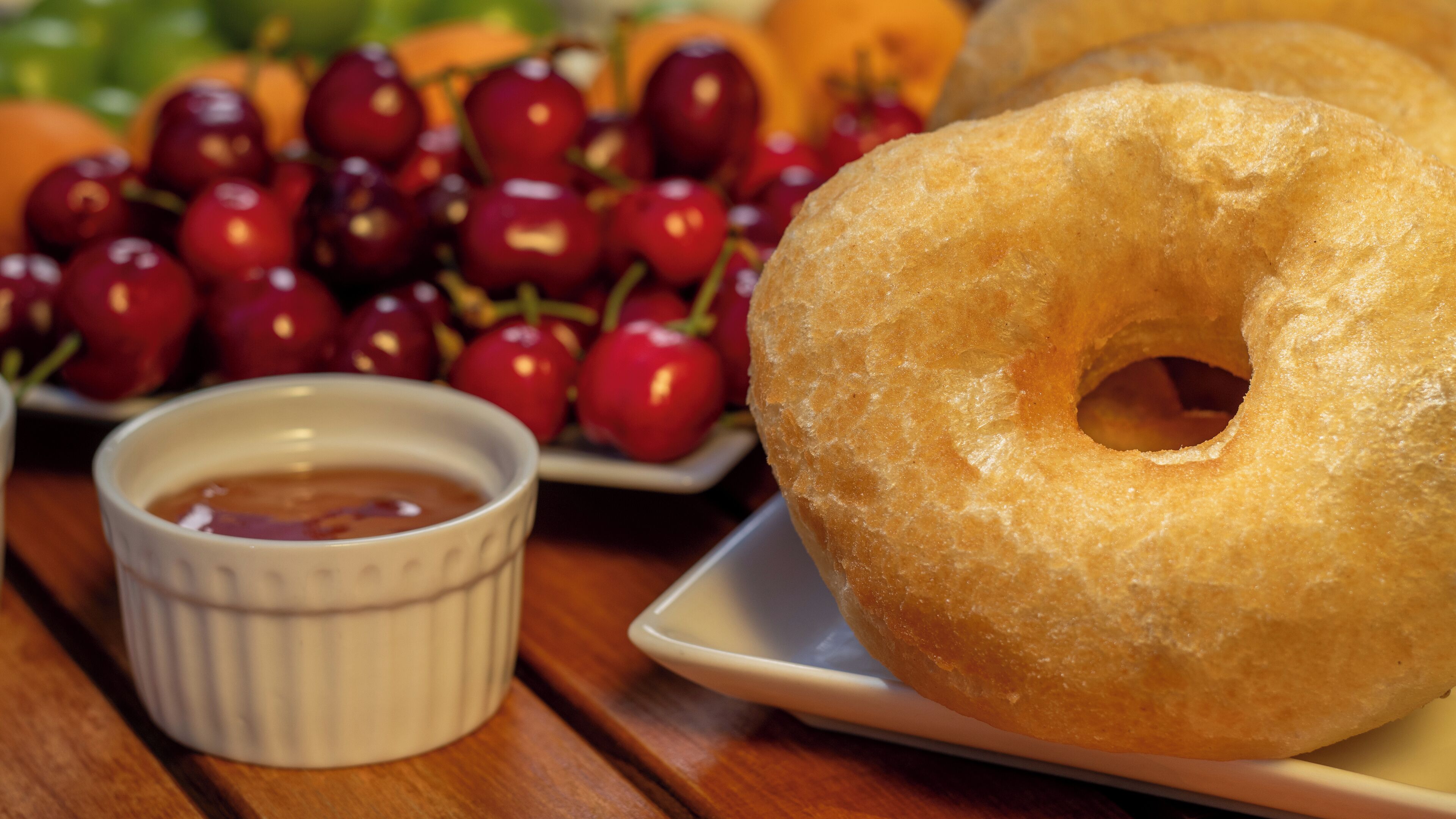 A plate with glazed donuts and a bowl of cherries.