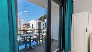 A balcony with a glass door, a table, and chairs, overlooking a pool and buildings.