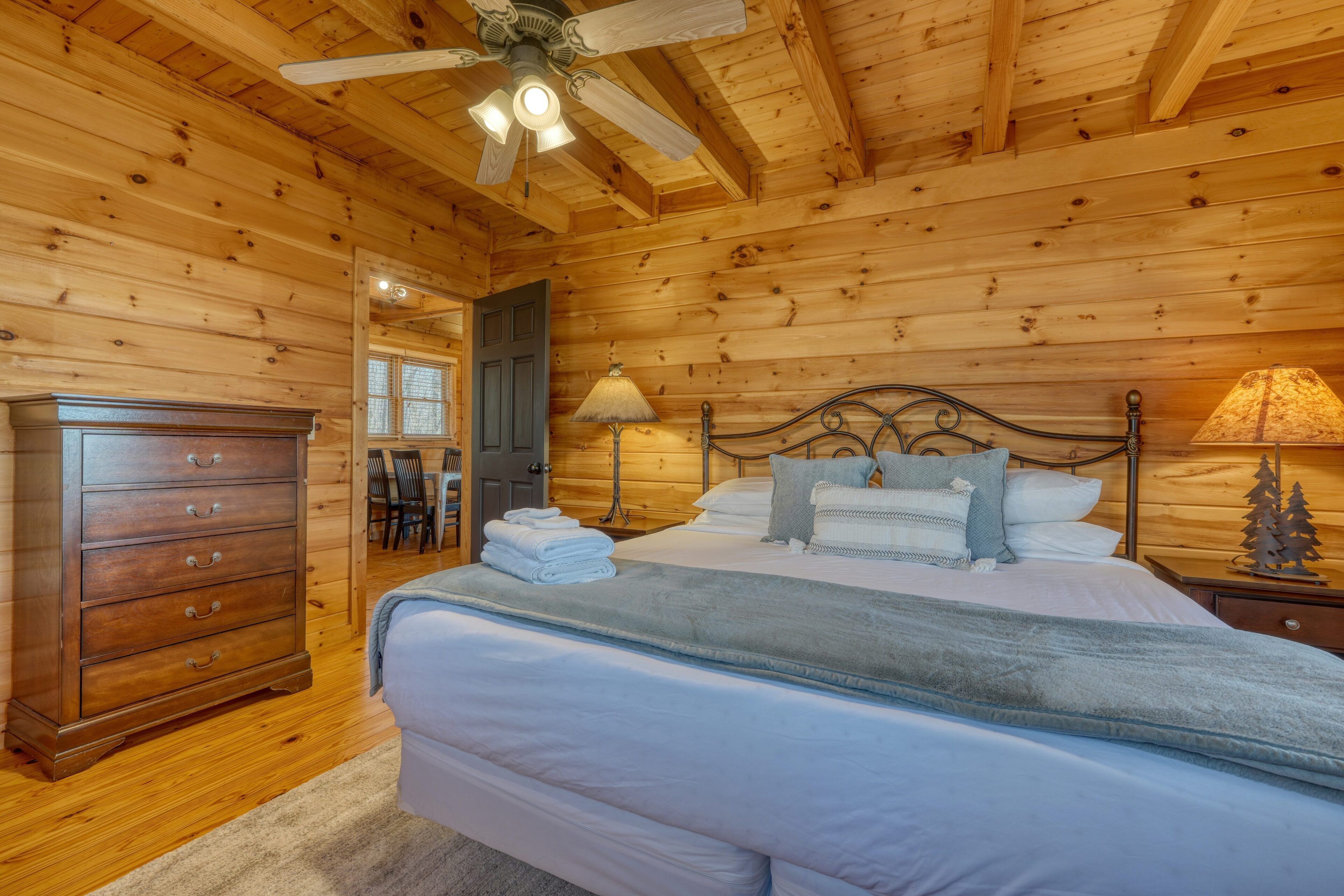 A wooden cabin bedroom with a bed, dresser, and ceiling fan.