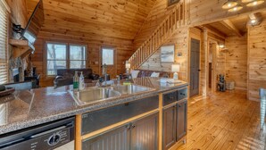 A wooden cabin interior with a kitchen area featuring granite countertops, stainless steel sinks, and a dishwasher. - Hidden Hills, Cabin for Family Getaway with Mountain Views! - Hot Tub and Wifi (Blairsville)