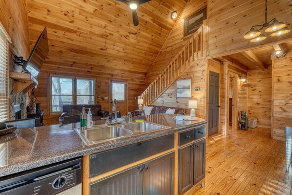 A wooden cabin interior with a kitchen area featuring granite countertops, stainless steel sinks, and a dishwasher. - Hidden Hills Sunset Soaks & Pizza Nights (Blairsville)