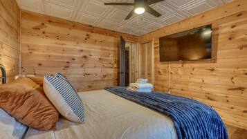 A wooden-paneled room with a bed, a ceiling fan, and a flat-screen TV mounted on the wall.