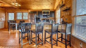 A wooden cabin interior with a kitchen area, dining table, and chairs. - Hidden Hills, Cabin for Family Getaway with Mountain Views! - Hot Tub and Wifi (Blairsville)