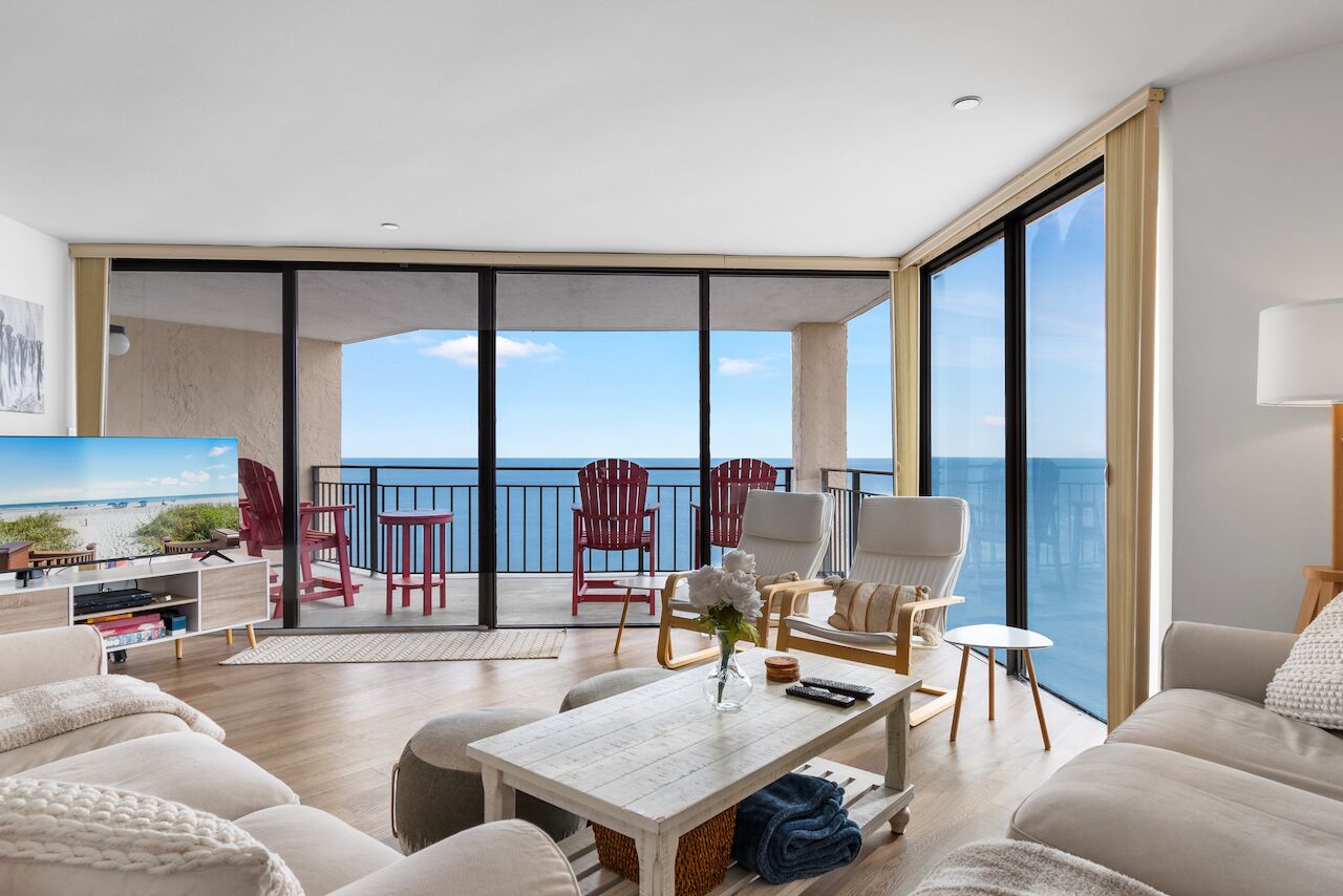 A spacious living room with a balcony overlooking the sea, furnished with modern chairs and a sofa.