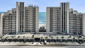 Un immeuble de grande hauteur doté de nombreux balcons, d’un espace de stationnement et offrant une vue sur la plage.