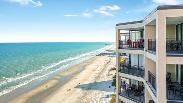 Un hôtel situé en bord de mer, doté de nombreux balcons, d’une plage de sable et offrant une vue dégagée sur l’océan.