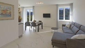 Un salon moderne avec un canapé gris, une table à manger avec des chaises, un téléviseur à écran plat et une grande fenêtre donnant sur les montagnes.