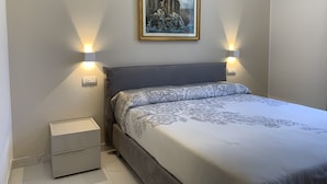 Une chambre à coucher avec un lit, une table de chevet, une lampe fixée au mur et un tableau encadré.