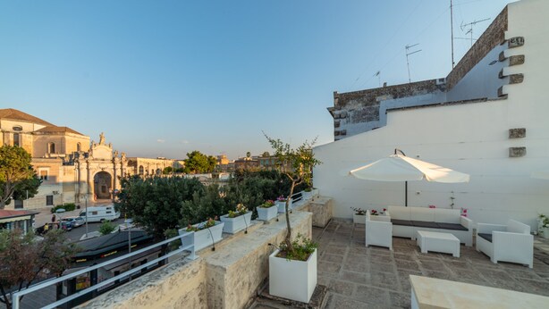 Eine Dachterrasse mit Außenmöbeln, Blumentöpfen und Blick auf die Stadtlandschaft.