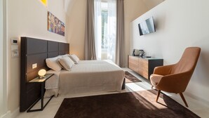 Ein modernes Hotelzimmer mit einem großen Bett, einem Flachbildfernseher, einem Holzschrank und einem bequemen Sessel.