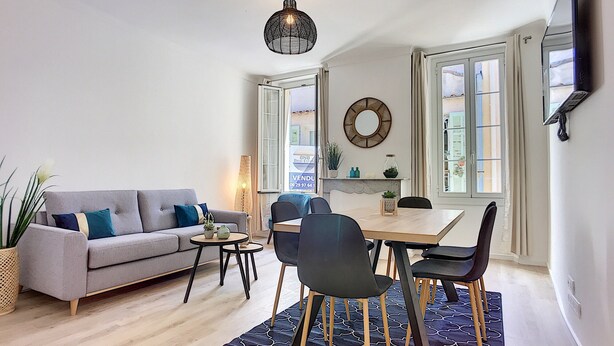 Una sala de estar moderna con un sofá gris, una mesa de comedor con sillas, un tapete estampado y una lámpara colgante.