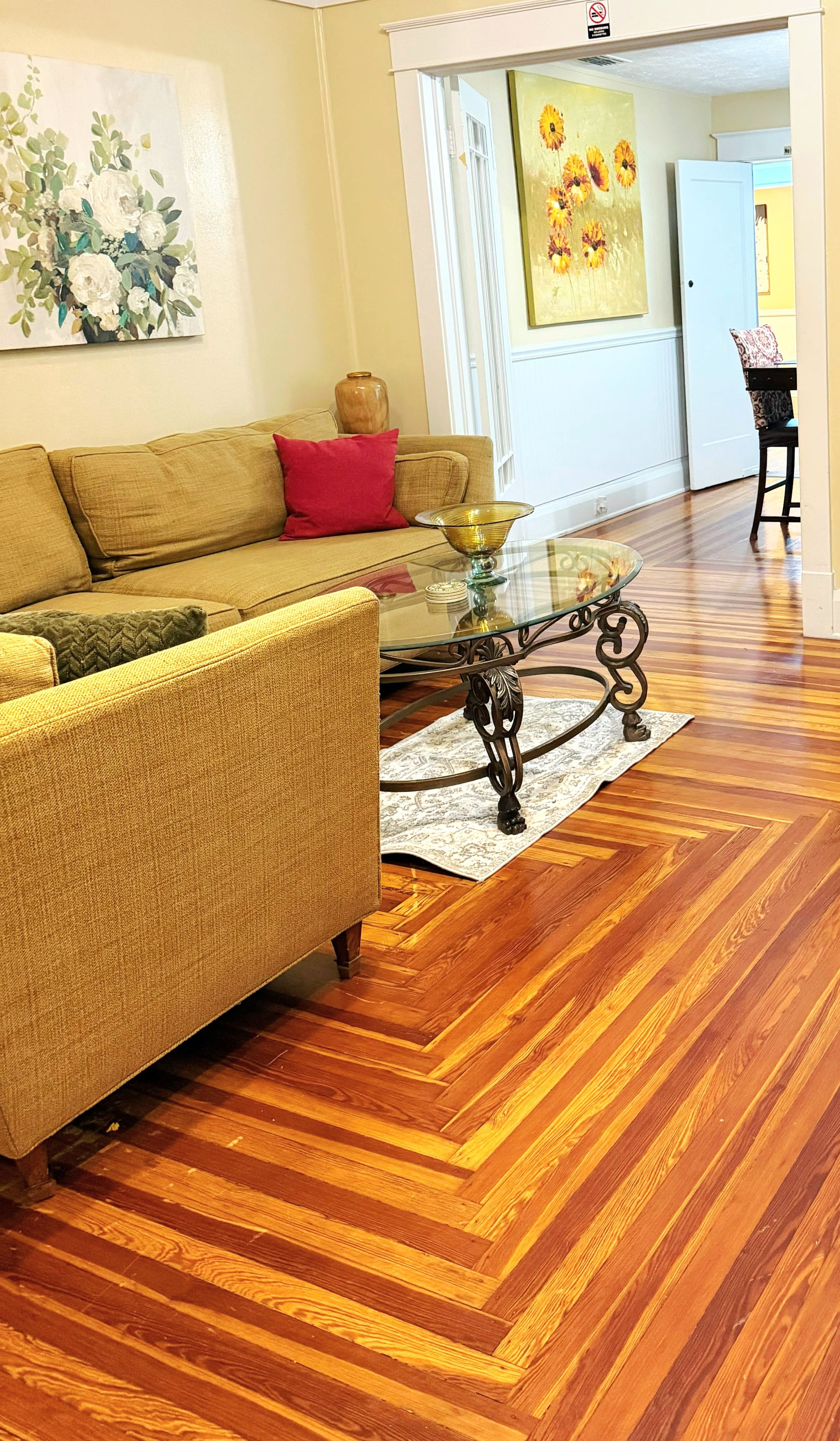 A living room with a sofa, a glass coffee table, and a patterned rug on a wooden floor.