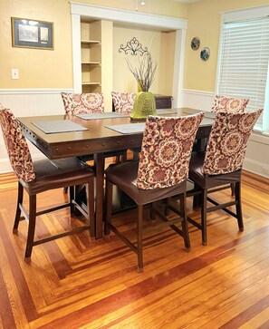 A dining room with a wooden table and patterned chairs, a vase with branches, and a decorative wall piece. - EXQUISITE FAMILY HOME (Lakeland)