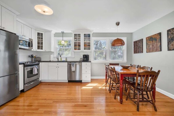 A modern kitchen with white cabinets, stainless steel appliances, and a wooden dining table with chairs.