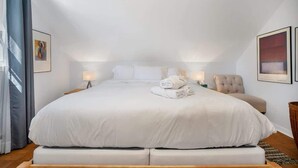 A bedroom with a large bed, two bedside lamps, a chair, and artwork on the walls. - Downtown Mystic House w/ Yard, Pet-Friendly Getaway (Mystic)