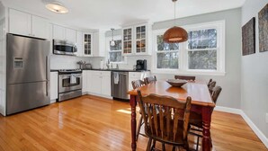 A modern kitchen with stainless steel appliances, white cabinetry, and a wooden dining table. - Downtown Mystic House w/ Yard, Pet-Friendly Getaway (Mystic)