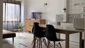 Cozinha moderna com área de refeições, com uma mesa de madeira, cadeiras pretas, uma TV e um painel de fundo de pedra.
