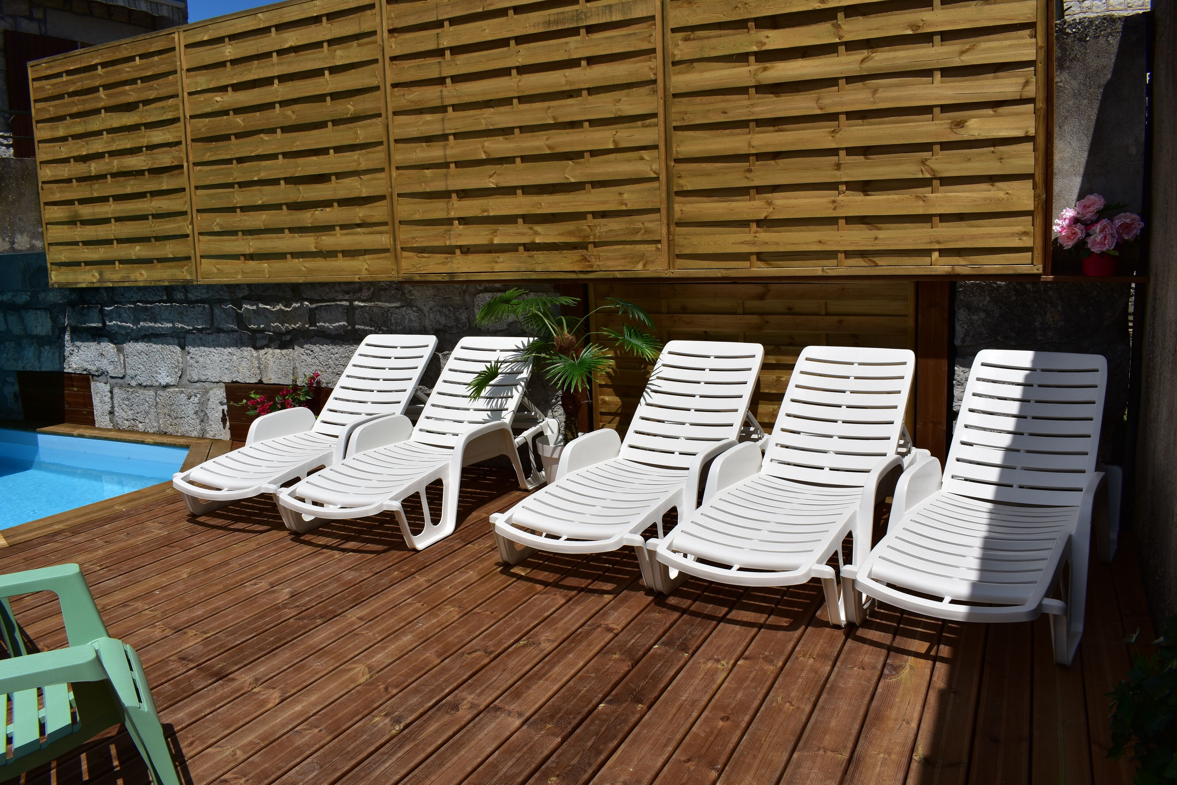 Eine Holzterrasse mit in einer Reihe angeordneten weißen Liegestühlen.