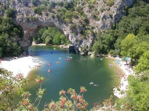 Un arco natural sobre una bahía tranquila con barcos y una playa arenosa.