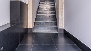 A staircase with a white wall and a black tiled floor leading to a landing. - Ortigia: A luxury apartment by the sea (Syracuse)
