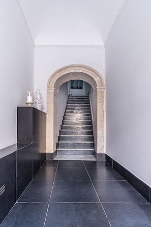Moderni portaikko, jonka yläosaan johtaa kivestä tehty kaarimainen holvikaari.