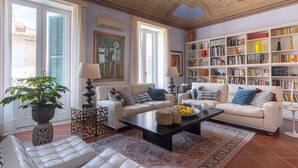 A spacious living room with white sofas, a black coffee table, and a bookshelf filled with books and decorative items. - Ortigia: A luxury apartment by the sea (Syracuse)