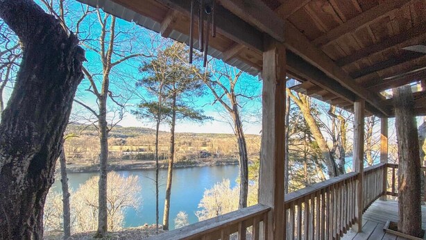 Une terrasse en bois avec une rambarde donnant sur une étendue d’eau et des arbres.