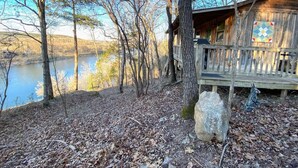 Une cabane au bord d’un lac, dotée d’une terrasse en bois et d’un grand rocher au premier plan.