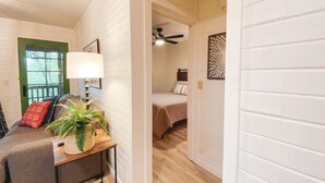 Une chambre avec un lit, une table de chevet avec une lampe, une fenêtre avec un cadre vert et un ventilateur de plafond.