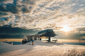 A ski lift station with a chairlift, snow-covered ground, and a building with a sloped roof.