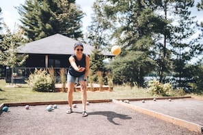 Henkilö pelaa shuffleboardia ulkona, taustalla näkyy talo.