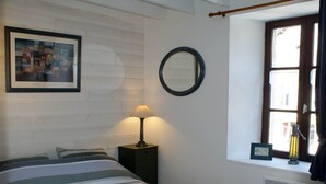 A hotel room with a bed, a bedside lamp, a window with a view, and a framed picture on the wall. - Maison au Coeur de Moncontour (Moncontour)