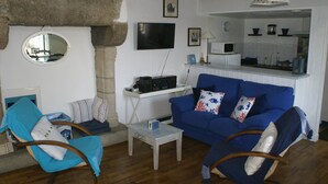 A living room with a blue sofa, a round mirror, a small table, and a stone pillar. - Maison au Coeur de Moncontour (Moncontour)